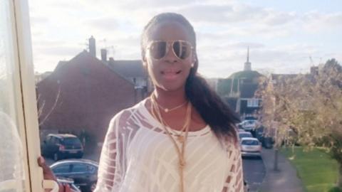 A woman in a white top with sunglasses smiles with a residential street visible behind her