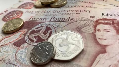 Silver and gold coins on top of several Manx £20 notes.