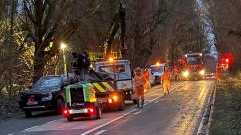 Works vehicles parked on a road lined with trees