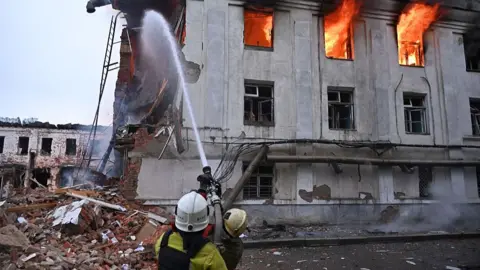 Two firefighters work to extinguish a fire in a three-storey building after a missile strike in Kharkiv, Ukraine