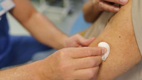 A close-up of male nurse pressing a piece of cotton wool on a man's arm after he has been vaccinated.