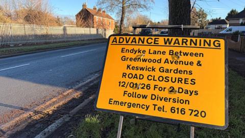An orange advanced warning of road closure on the grass verge by the side of Endike Lane in Hull