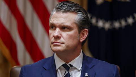 Pete Hegseth, wearing a blue suit, blue and white striped neck tie and a lapel pin, during a meeting at the White House.