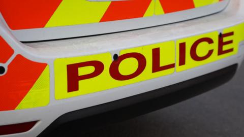 The back of a police car. There are fluorescent orange and yellow markings with the word police in capital letters.