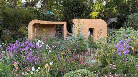 A view of part of the 'Silent No More' garden. There are purple, white and pink flowers around two wooden blocks at the centre. 