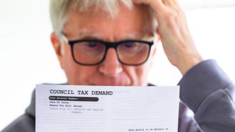 Man in glasses reads a council tax demand.