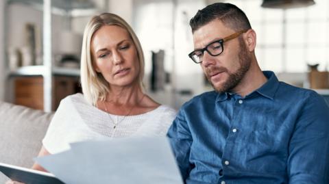 Shot of a couple sitting in their lounge reviewing bills while using a digital tablet - stock photo