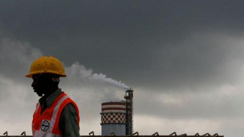 A worker stands in front of a chemical factory as it discharges exhaust into the air of Mumbai, India, on Monday, Sept. 13, 2010.