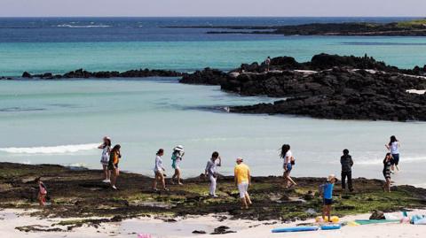 Tourists walking on a white sand beach under the sun in Jeju Island South Korea