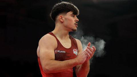 Gabriel Langton claps his hands covered with chalk while wearing a red England vest