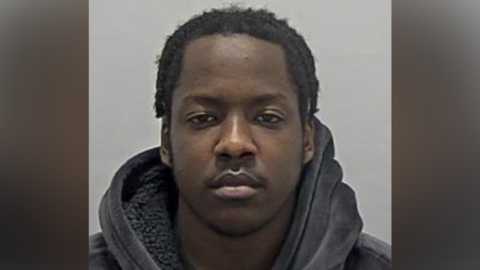 Ahmed Adam in police custody, wearing a fluffy black hoodie.