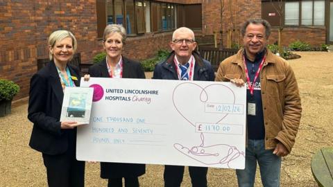Two women and two men standing outside a building holding a giant cheque made out to United Lincolnshire Hospitals Charity. 