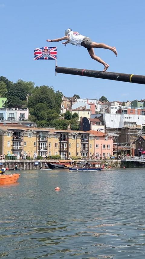A man is launching off a pole into the water below.