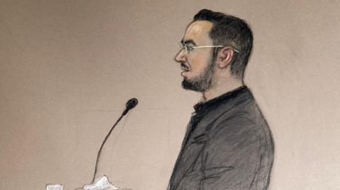 A court sketch of Pouria Zeraati giving evidence in the trial of two men accused of stabbing him. He has black hair and a black beard and is wearing a grey suit jacket.