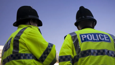 Two police officers, seen from behind, wearing yellow hi-vis hjackets and traditional black police hats.
