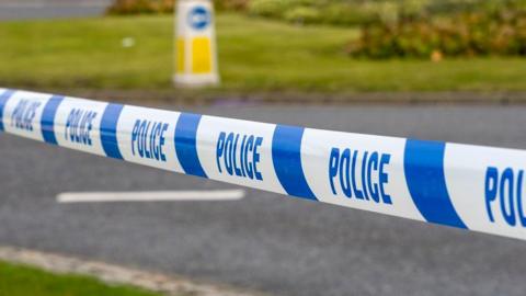 Stock image of a scene of a crash, with a police cordon in front of a road