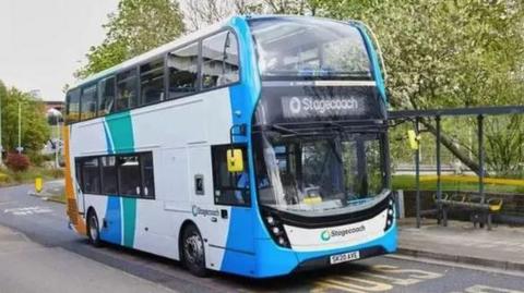 A blue and white Stagecoach double decker bus parked at a bus stop with a driver in the front seat.