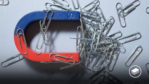 A photograph of lots of metallic paper clips on a horseshoe magnet.
