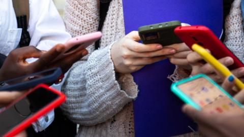 Various teenagers all holding mobile phones
