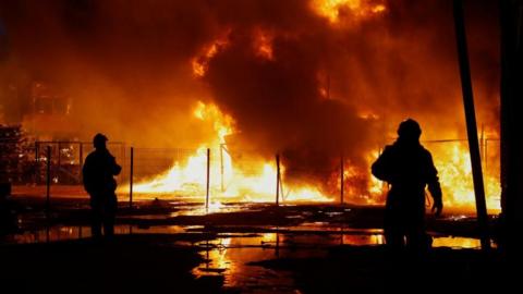 Two rescuers are silhouetted against a backdrop of fire in Kyiv