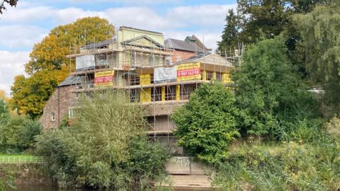 A building covered in scaffolding and surrounded by green leafy trees