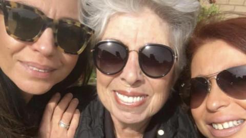 Three women wearing sunglasses smile at the camera.