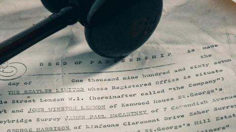 A photograph of one of the legal documents, bearing the names and addresses of John Lennon, Paul McCartney and George Harrison, along with an auctioneer's gavel. 