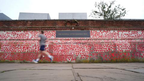 A jogger runs past the Covid Memorial Wall, central London. The wall is covered in red love hearts