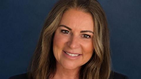 Restore Britain candidate, Rebecca Shepherd. She has shoulder-length dark hair, is wearing a dark blazer and a white blouse. 
