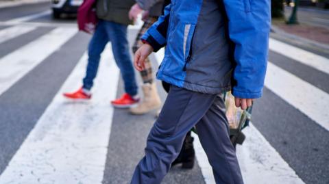 The image shows the midsection of pedestrian adult men walking across a pedestrian crossing.