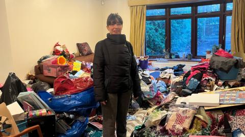 Nevena Khediri pictured at her family home in Camberley, Surrey, which is full of rubbish. Nevena is stood in the middle of the image in front of huge piles of rubbish
