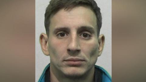 Mugshot of Smith. He is clean shaven with neat short brown hair.