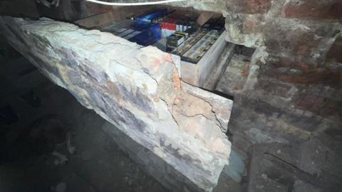 A brick stone wall has a hidden drawer in the middle of it. A section of brick is sticking out with a drawer inside full of cigarettes. 