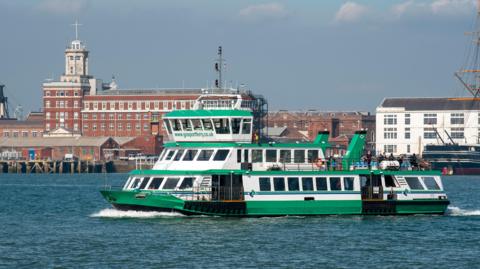 The Gosport Ferry pictured in motion on the water. The ferry, which has "www.gosportferry.co.uk" printed on the front, is painted white and green.