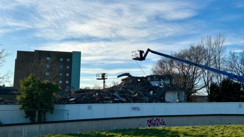 The demolition of Castle Leazes. A pile of rubble can be seen beneath a blue crane; an apartment block stands in the background, to the left.