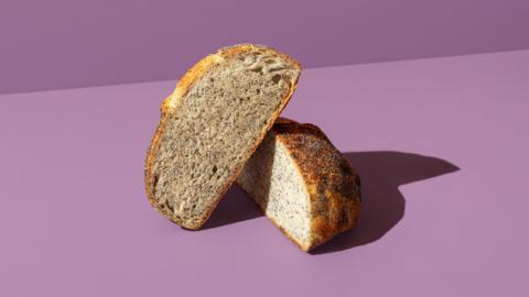 A seeded loaf of bread cut in half on a purple background