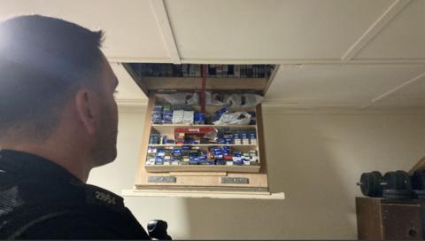 Several cigarettes located on shelves are hanging down from a ceiling. A police officer can be seen in the corner of the image looking at the cigarettes.
