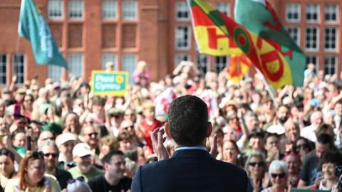 rhyn ap iorwerth from behind looking out on a crowd of people in front of the senedd.