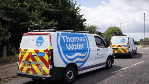Two Thames Water-branded vans on a road. A hedge is visible in the background. 