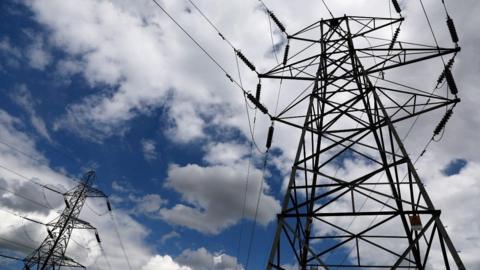 Electricity pylons against a blue sky with fluffy white clouds.