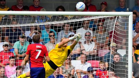 The Bristol Rovers goalkeeper dives high to the right to push the ball over the bar from a York City player.