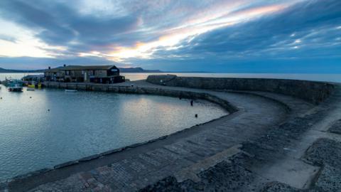 The Cobb stretching out to sea in the early evening. A building is visible at one end.