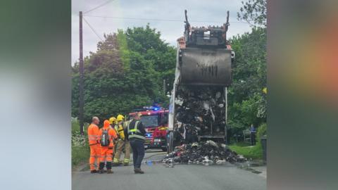 A lorry with burnt waste spilling out on to a village road