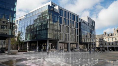 The Marischal Square development in Aberdeen, a large glass building, with small fountains in the foreground.