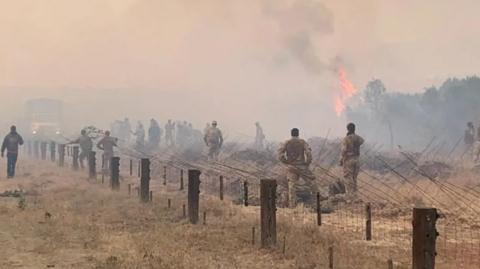 A photo of a number of soldiers looking at a fire in front of them