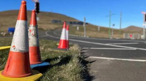 A set of orange cones with white stripes, there is a bridge in the background at the Bungalow, and you can see the peak of the hill.