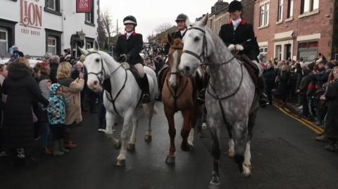 Riders with their hard hats and hunting outfits from The Holcombe Harriers hunt ride through the streets of  Wheelton, Lancashire opposdite the RTed Lion Inn.