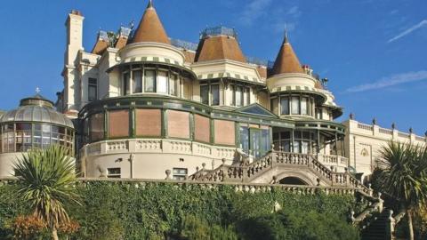 The Russell Cotes Museum - a Victorian building with turrets and external staircases set against a blue sky with palm trees in the foreground