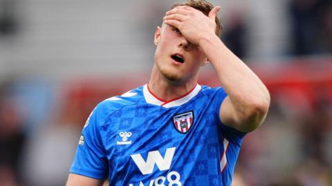 Sunderland's Daniel Ballard holds his forehead, wearing his team's away shirt, which is blue with a repeated pattern depicting a lighthouse through a circular structure