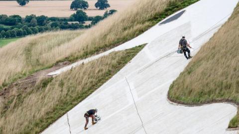 Two men abseiling down the front of a large white horse on a hillside